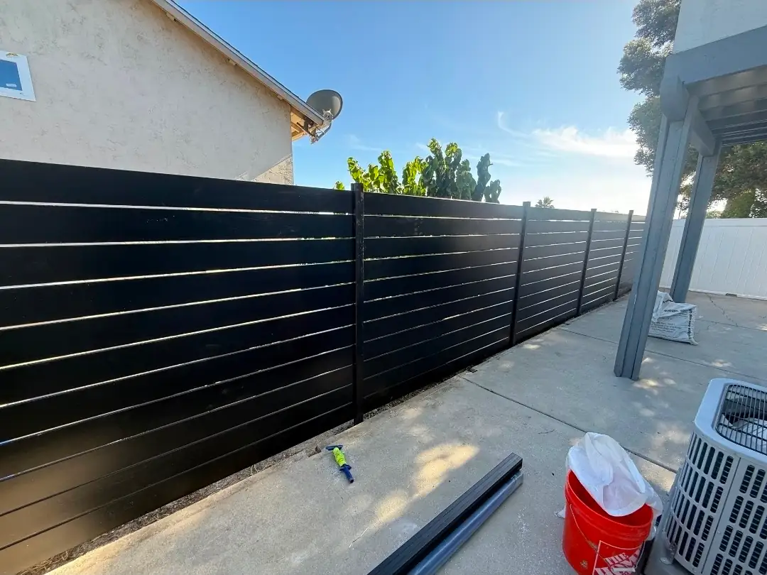 Wide view of custom black aluminum slat privacy fence installed at a San Diego home